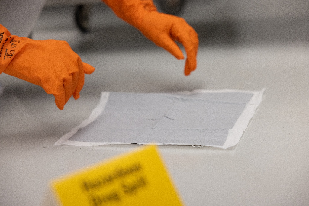 hands in orange gloves over matt with gray sheet over it