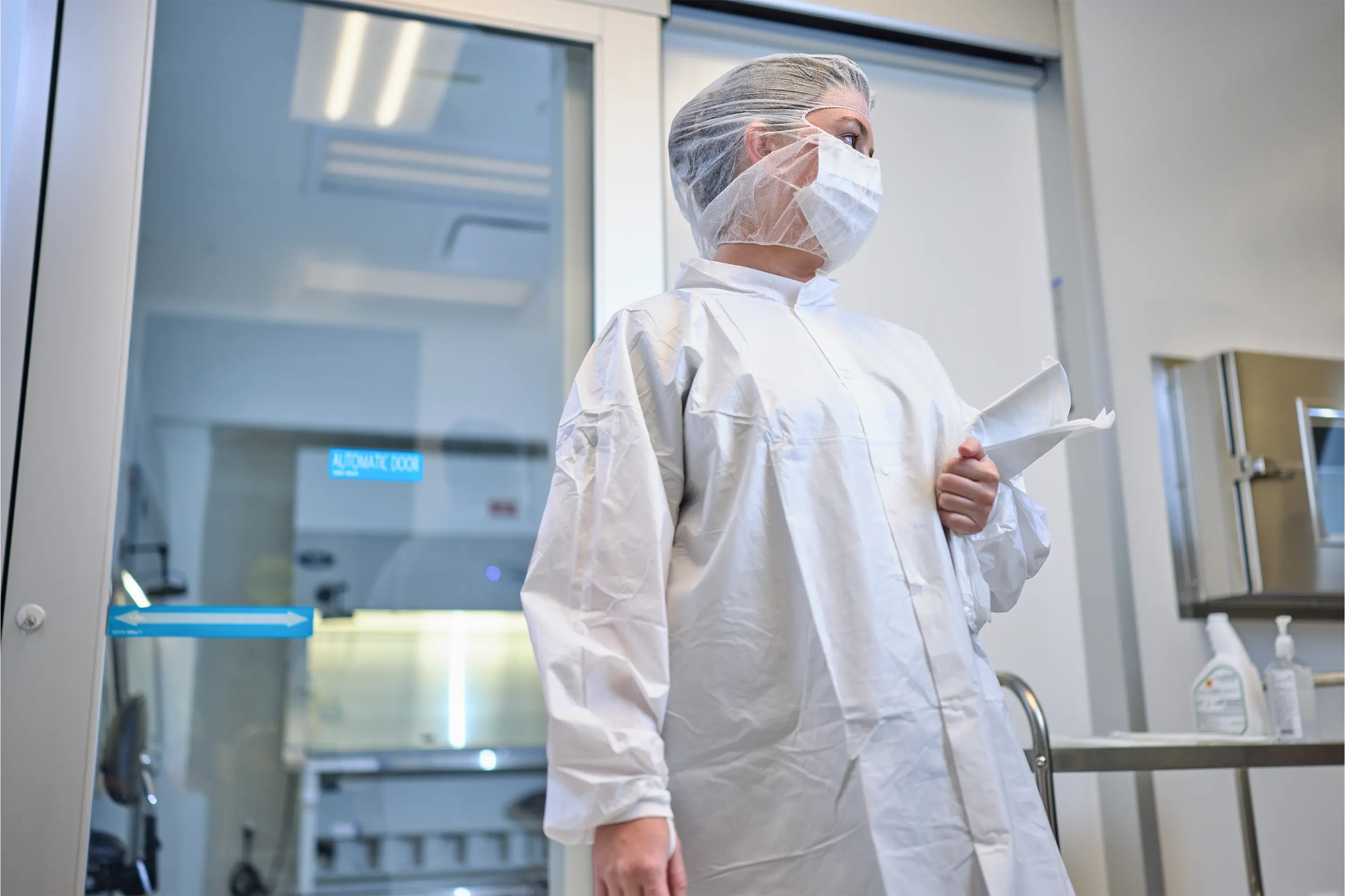 Operator wearing protective cleanroom garments standing in a hazardous drug compounding environment.