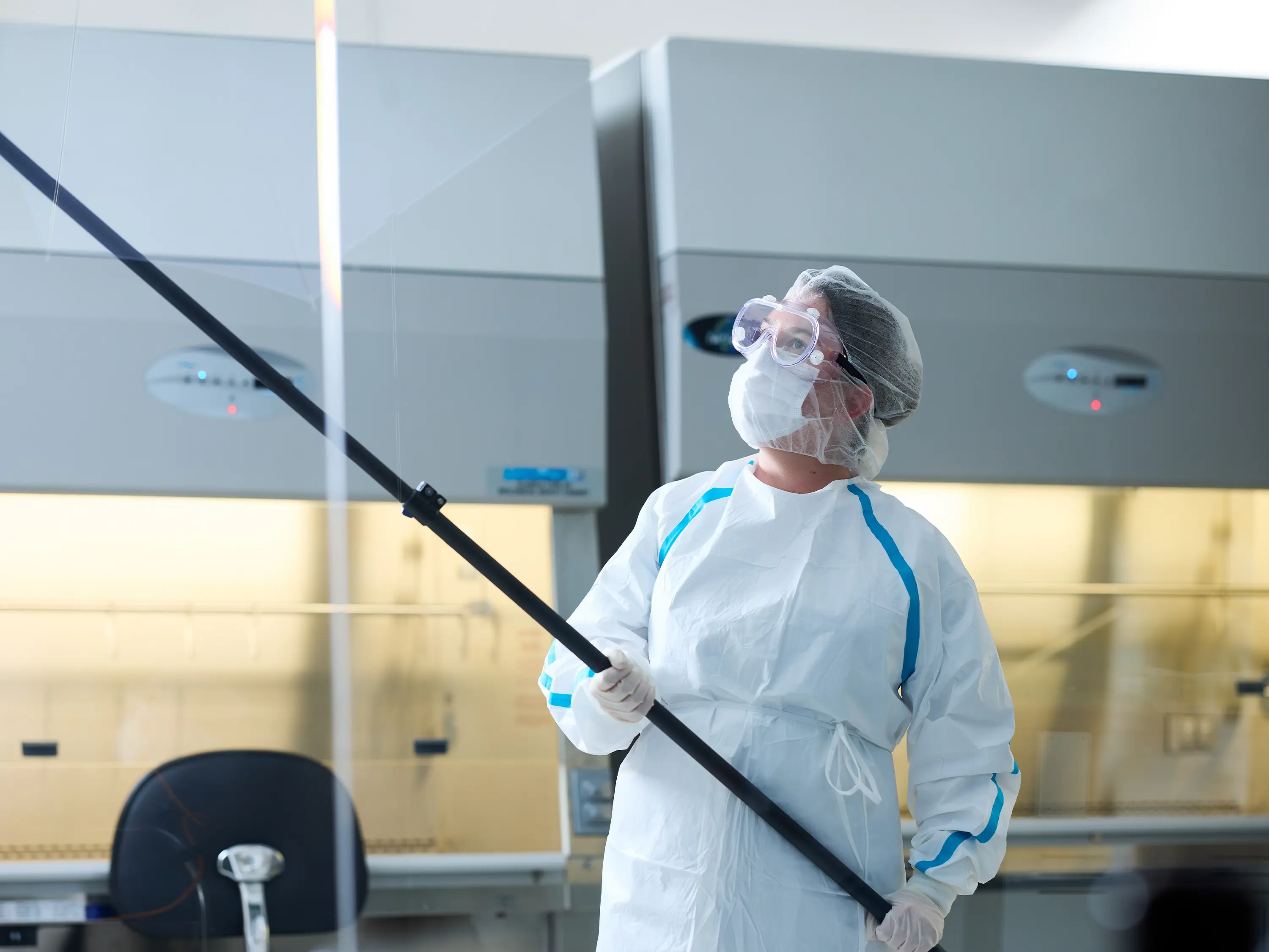 Operator in protective cleanroom garments mopping a wall in a hazardous drug cleanroom.